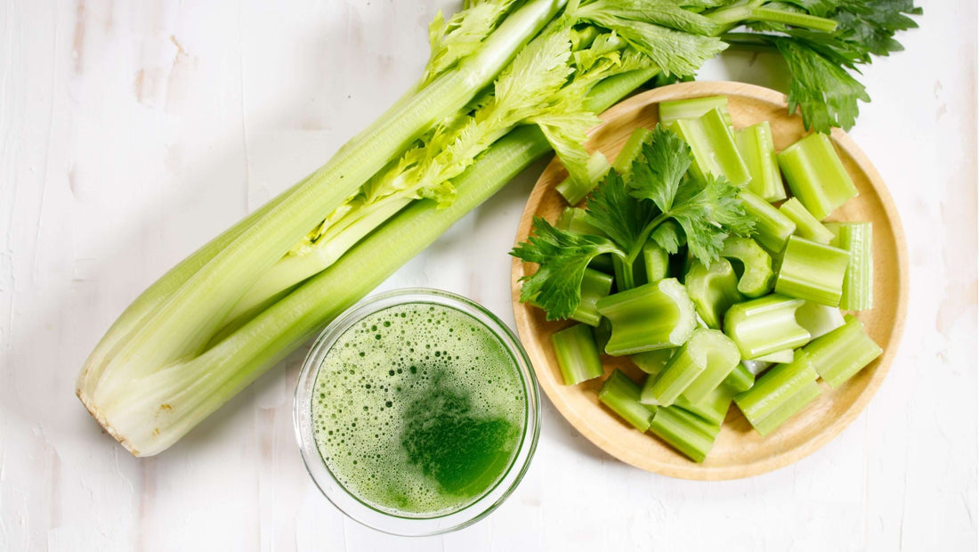 Bunch of celery and some chopped next to a glass of fresh celery juice.