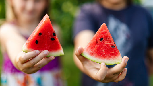 Two kids holding a slice of fresh, seeded watermelon to the camera