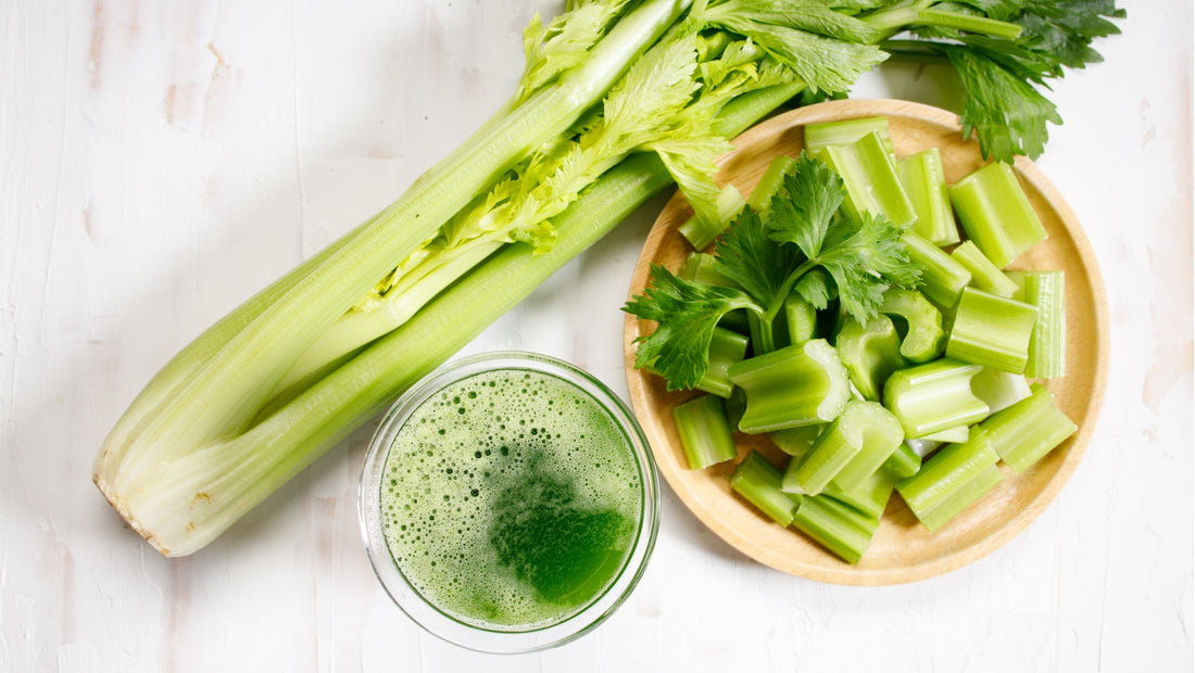 Bunch of celery and some chopped next to a glass of fresh celery juice.