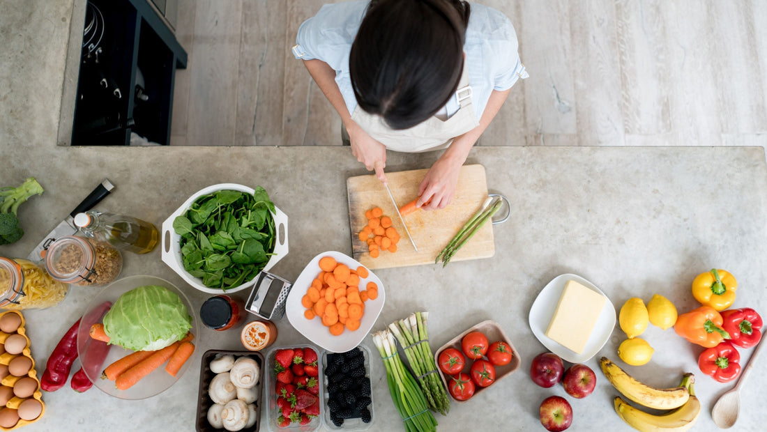Woman meal prepping with various fresh fruit, vegetables, eggs, pasta, butter and sauces in kitchen.