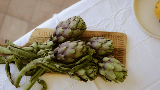 Bunch of fresh organic, locally grown artichokes on chopping board.