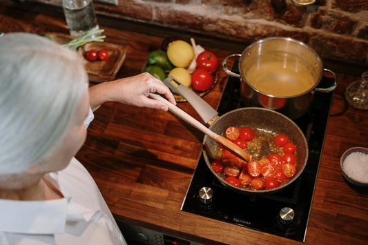Grandmother cooking tomatoes in kitchen stovetop next to lemons, limes, garlic and other vegetables.